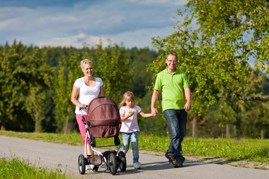 Family with two children (the baby lying in a baby buggy) walking down a path outdoors