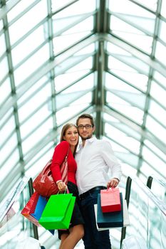 Couple - man and woman - in a shopping mall with colorful bags on an escalator