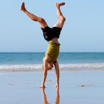 Young sportive man doing gymnastics on the beach