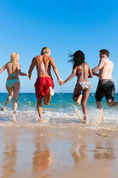 Four friends - men and women - on the beach having lots of fun in their vacation running through the water