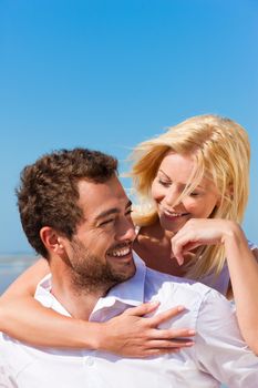 Couple in love - Caucasian man having his woman piggyback on his back under a blue sky on a beach