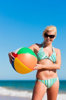 Attractive Woman in bikini standing in the sun on beach under a blue sky