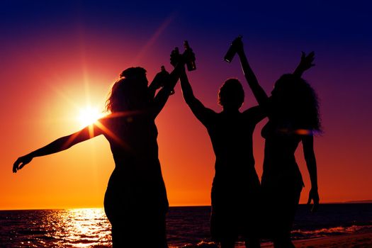 People (two couples) on the beach having a party, drinking and having a lot of fun in the sunset (only silhouette of people to be seen, people having bottles in their hands with the sun shining through)