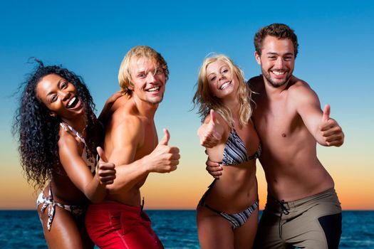 People (two couples) on the beach having a party, dancing and having a lot of fun in the sunset