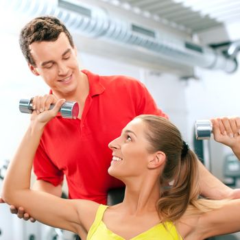 Young woman lifting a dumbbell in the gym assisted by her personal trainer (focus on woman)