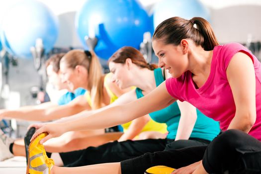 Group of four people in colorful cloths in a gym doing aerobics or warming up with gymnastics and stretching exercises