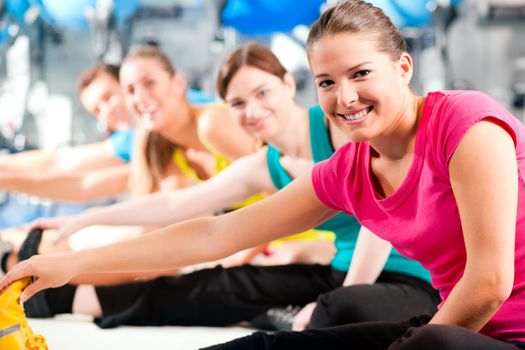 Group of four people in colorful cloths in a gym doing aerobics or warming up with gymnastics and stretching exercises