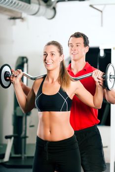 Woman in gym with personal fitness trainer exercising power gymnastics with a barbell