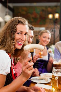 group of young men and women in traditional Bavarian Tracht having a breakfast with white veal sausage, pretzel, and beer