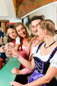 People in Bavarian Tracht drinking hard liquor in a pub and have fun