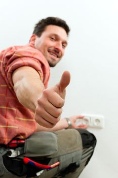 Electrician installing a power socket giving the thumbs-up sign - focus on thumb