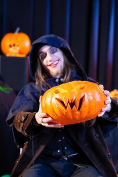 Man in scary Halloween costume holding pumpkin