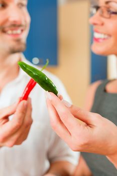 Young couple - man and woman - cooking in their kitchen at home, they teasing each other