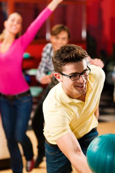 Group of three friends in a bowling alley having fun, two of them cheering the one in charge to throw the bowling ball