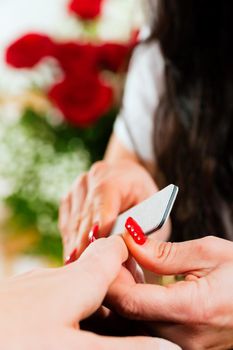 Woman in a nail salon receiving a manicure by a beautician, lots of roses in the background