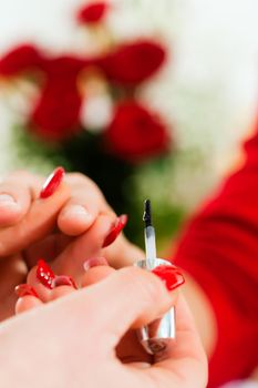 Woman in a nail salon receiving a manicure by a beautician, lots of roses in the background