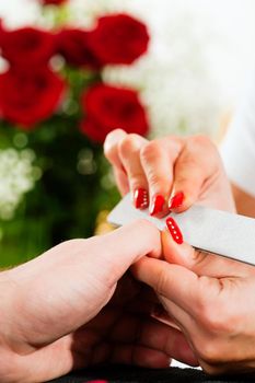 Man in a nail salon receiving a manicure by a beautician, lots of roses in the background