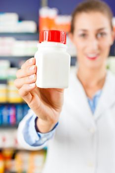 Female pharmacist is standing in her drugstore behind the counter holding a medicine bottle