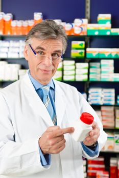 Pharmacist in pharmacy, he is holding a bottle with pharmaceuticals in his hand