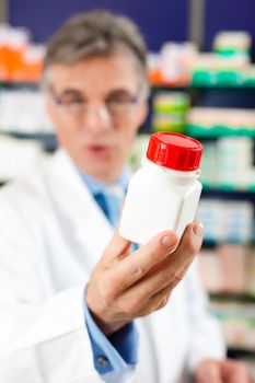 Pharmacist in pharmacy, he is holding a bottle with pharmaceuticals in his hand