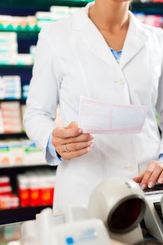 Female Pharmacist in pharmacy, standing at the cashier she is holding a prescription slip in her hands