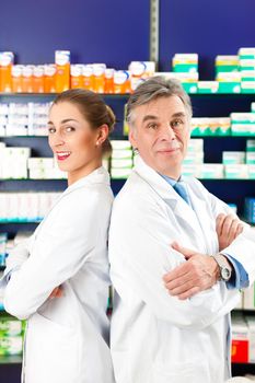 Two Pharmacists standing in pharmacy or drugstore in front of shelves with pharmaceuticals