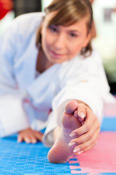 Woman in martial art training in a gym, she is stretching and warming up