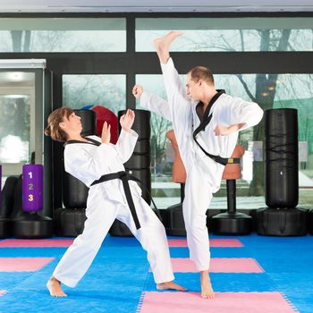 People in a gym in martial arts training exercising Taekwondo, both have a black belt