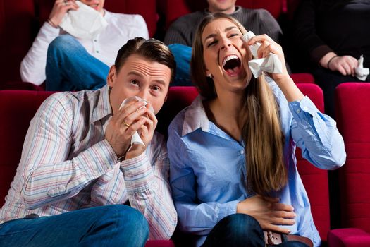 Couple and other people, probably friends, in cinema watching a movie, it seems to be a funny movie