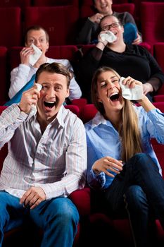 Couple and other people, probably friends, in cinema watching a movie, it seems to be a funny movie