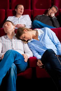 Couple and other people, probably friends, in cinema watching a movie, it seems to be a boring movie