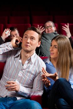 Couple and other people, probably friends, in cinema watching a movie, one is making a phone call and bothering the others