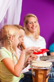 Family - Children and mother - making music, at home, they are practicing playing guitar, bongo and flute as instruments
