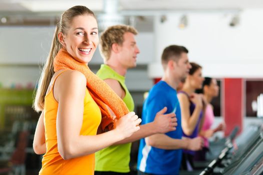 Running on treadmill in gym or fitness club - group of women and men exercising to gain more fitness