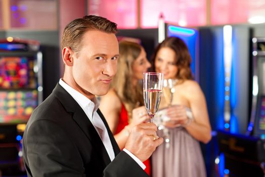 Three friends with champagne in a bar or casino, a man is looking in the camera