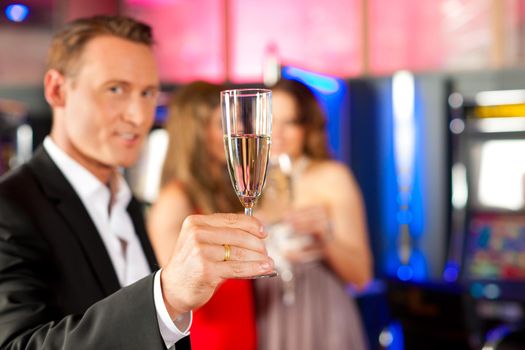 Three friends with champagne in a bar or casino, a man is looking in the camera