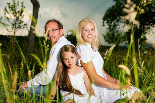 Happy family with daughter girl sitting in a meadow in summer before a storm