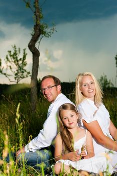 Happy family with daughter girl sitting in a meadow in summer before a storm