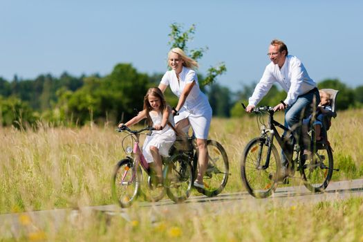Family with baby and girl child having a weekend excursion on their bikes on a summer day in beautiful landscape