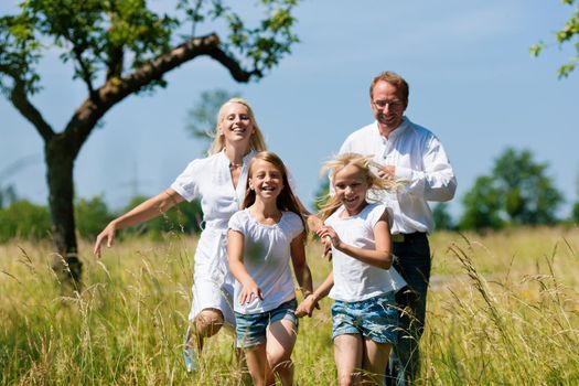 Happy Family with two girls running in a meadow in summer