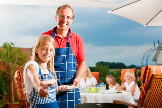 Happy family having a barbecue in summer; the father and a child standing at the grill