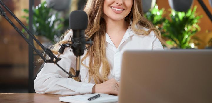 Close up of smiling beautiful woman in white shirt communicating online with microphone and laptop. Concept of process live broadcast for followers and telling interesting information. 