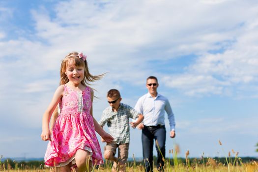 Happy family - father, children - playing on a meadow in summer under blue sky