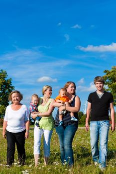 Family and multi-generation - mother, father, children and grandmother having fun on meadow in summer