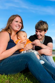 Family - mother, father and child sitting and playing in garden