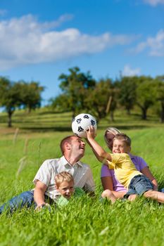 Family with two little boys playing in the grass on a summer meadow - they have a football