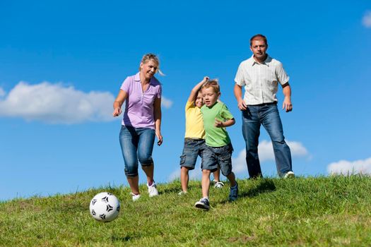 Happy family with two little boys playing soccer in the grass on a summer meadow