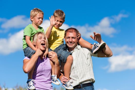 Family with two little boys on a summer meadow - the parents carry the sons on their shoulders