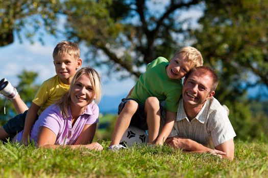 Family with two little boys playing in the grass on a summer meadow - they have a football