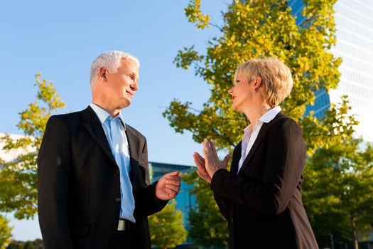 Business people - mature or senior - standing in a park outdoors talking